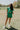 Full body front view of female model wearing the Paulina Green Quilted Shorts that have green quilted fabric, a drawstring elastic waist, and side pockets. Worn with matching top
