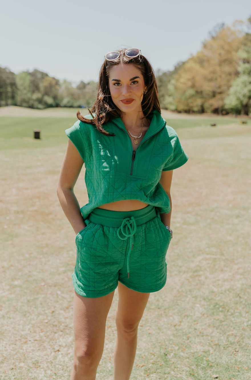 Front view of female model wearing the Paulina Green Quilted Shorts that have green quilted fabric, a drawstring elastic waist, and side pockets. Worn with matching top
