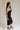 Full body side view of female model wearing the Marissa Black & White Trim Midi Dress which features Black Lightweight Fabric, Midi Length, Black Lining, White Trim Details, Back Slit , Square Necklineand Side Monochrome Zipper with Hook Closure