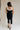 Full body back view of female model wearing the Marissa Black & White Trim Midi Dress which features Black Lightweight Fabric, Midi Length, Black Lining, White Trim Details, Back Slit , Square Necklineand Side Monochrome Zipper with Hook Closure