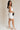 Full body side view of female model wearing the Taylor Off White Bow Cut-Out Mini Dress which features White Lightweight Fabric, White Lining, Mini Length, Square Neckline, Side Zipper with Hook Closure and Bow Cut-Out Back Detail
