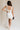 Full body back view of female model wearing the Taylor Off White Bow Cut-Out Mini Dress which features White Lightweight Fabric, White Lining, Mini Length, Square Neckline, Side Zipper with Hook Closure and Bow Cut-Out Back Detail