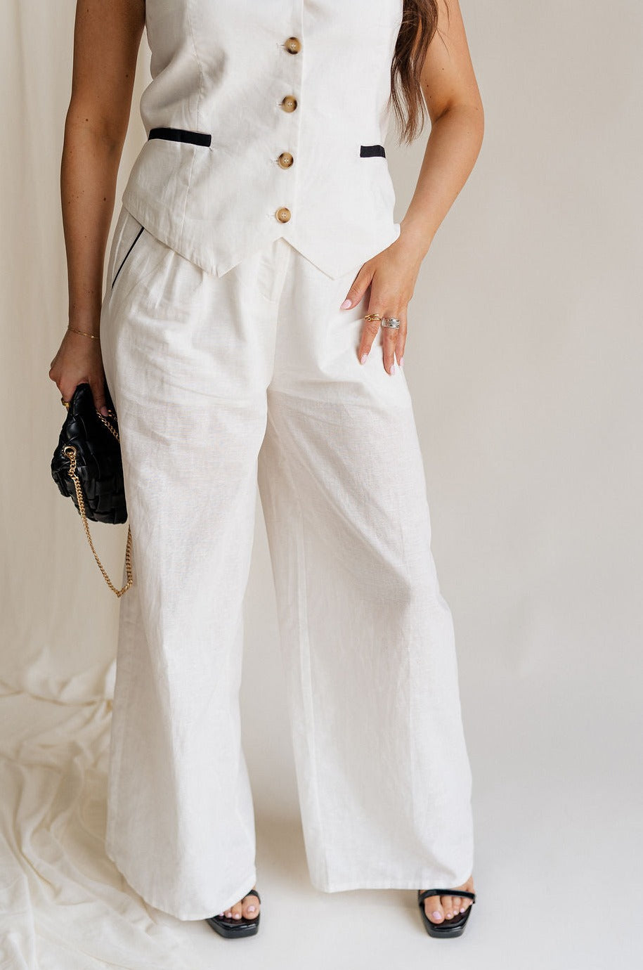 fronnt view of female model wearing the Amelia Off White & Black Wide Leg Pants which features Off White Linen Fabric, Black Trim Details, Front Pockets, Wide Pant Legs, Front Zipper with Tortoise Button Closure and Belt Loops
