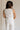 back view of female model wearing the Amelia Off White & Black Button-Up Vest which features White Linen Fabric, Black Trim Details, Front Pockets, Brown Tortoise Button Up, V-Neckline and Sleeveless