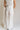 back view of female model wearing the Amelia Off White & Black Wide Leg Pants which features Off White Linen Fabric, Black Trim Details, Front Pockets, Wide Pant Legs, Front Zipper with Tortoise Button Closure and Belt Loops
