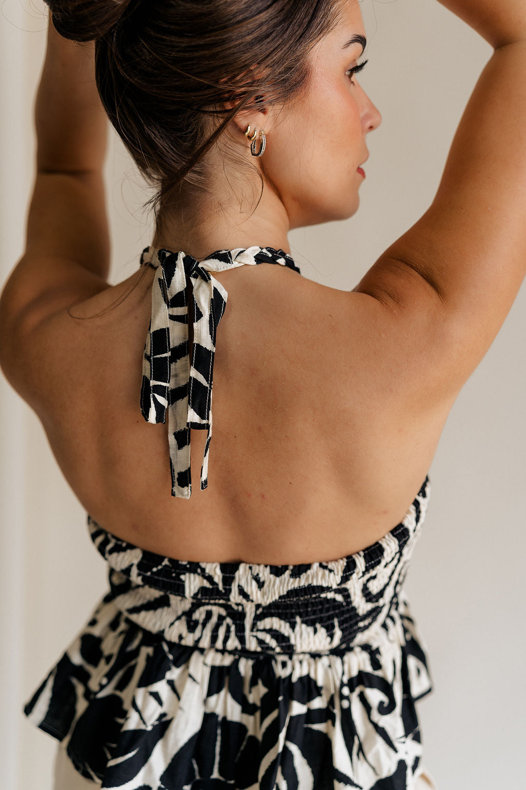back view of female model wearing the Olivia Black & White Swirl Braided Halter Tank which features Black and Cream Floral Fabric, Peplum Body, Ruched Upper, Braided Halter Neckline and Smocked Back