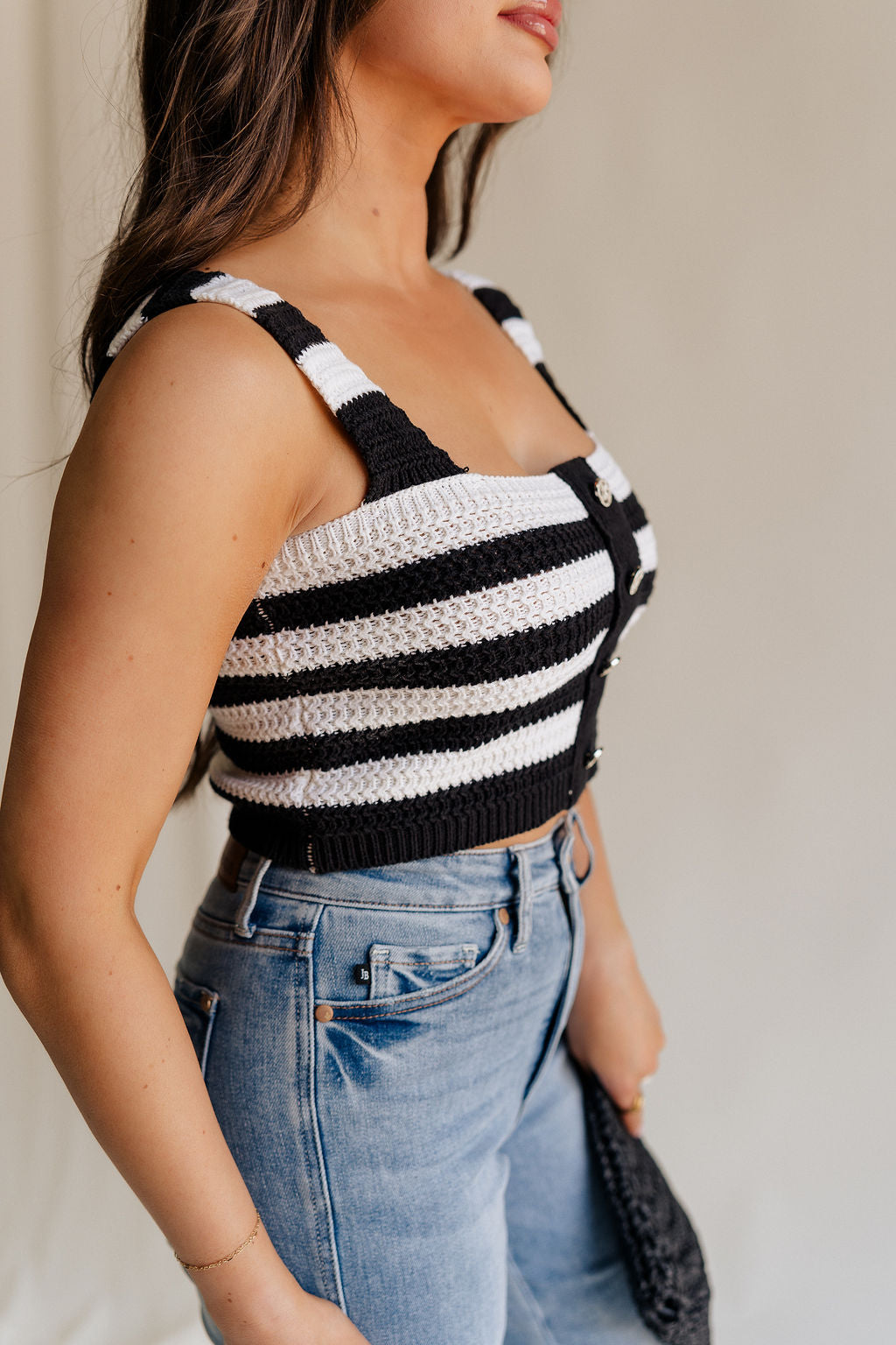 side view of female model wearing the Kai Black & White Stripe Knit Tank which features Black and White Crochet Knit, Stripe Pattern, Cropped Waist, Rhinestone Button Up, Square Neckline and Sleeveless
