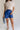 Lower body front view of model wearing the Mara Blue High Waist Shorts that have blue fabric, a high-rise elastic back waist. Worn with beige top.
