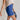 Close side view of model wearing the Mara Blue High Waist Shorts that have blue fabric, a high-rise elastic back waist. Worn with beige top.