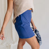 Close side view of model wearing the Mara Blue High Waist Shorts that have blue fabric, a high-rise elastic back waist. Worn with beige top.