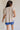 back viiew of female model wearing the Arana Knit Short Sleeve Top which features Lightweight Knit Fabric, Slight Slit Details, Front Left Chest Pocket, Round Neckline and Short Sleeves. the top is available in beige and mauve