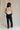 Full body back view of female model wearing the Remi Rhinestone Slit Black Jeans that have black denim, thigh slits with rhinestone trim, and pockets.