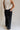 Lower body back view of female model wearing the Remi Rhinestone Slit Black Jeans that have black denim, thigh slits with rhinestone trim, and pockets.