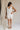 Full body back view of female model wearing the Monroe Off White Satin Tank Top that has off white satin fabric and a v-neckline.