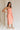 Full body frontal side view of female model wearing the Reyna Peach Ruffle Strapless Midi Dress, that has peach fabric, a strapless neck, a ruffle detail, and midi length hem.