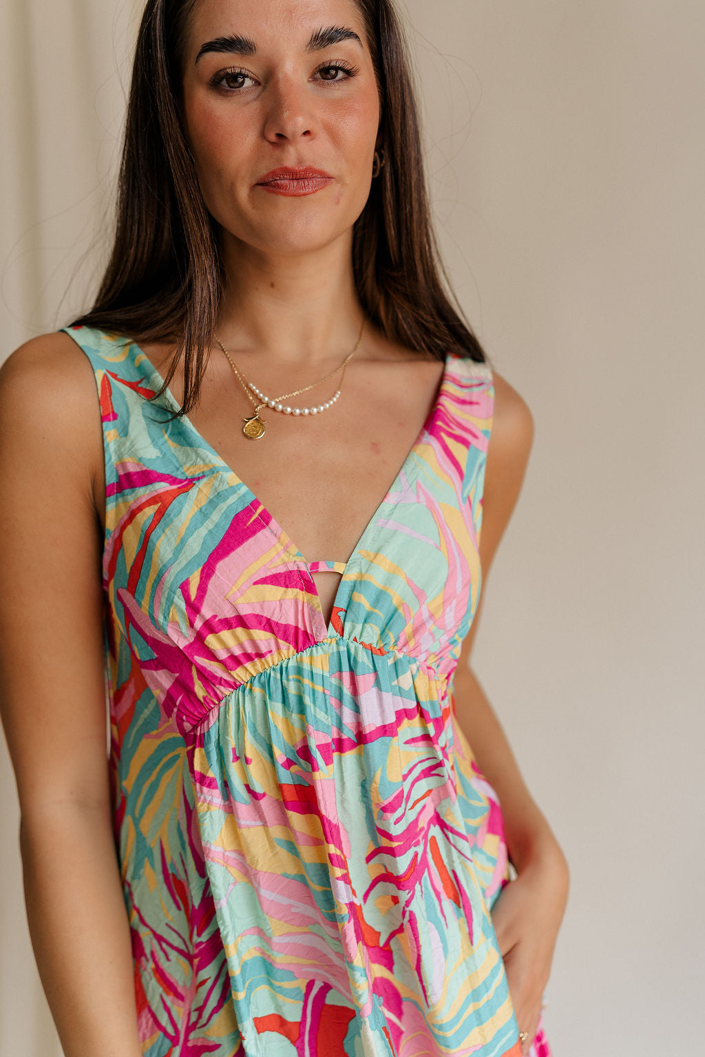 Upper body front view of female model wearing the Florence Floral Print Sleeveless Mini Dress that has a colorful floral palm print, v neck and back, and mini length.