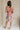 Full body back view of female model wearing the Florence Floral Print Sleeveless Mini Dress that has a colorful floral palm print, v neck and back, and mini length.