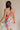 Back view of female model wearing the Florence Floral Print Sleeveless Mini Dress that has a colorful floral palm print, v neck and back, and mini length.