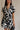 Close-up front view of model wearing the Melanie Black & Cream Printed Romper that has black and cream fabric with a swirl print, a button up front, collar, tie belt, and short sleeves. 