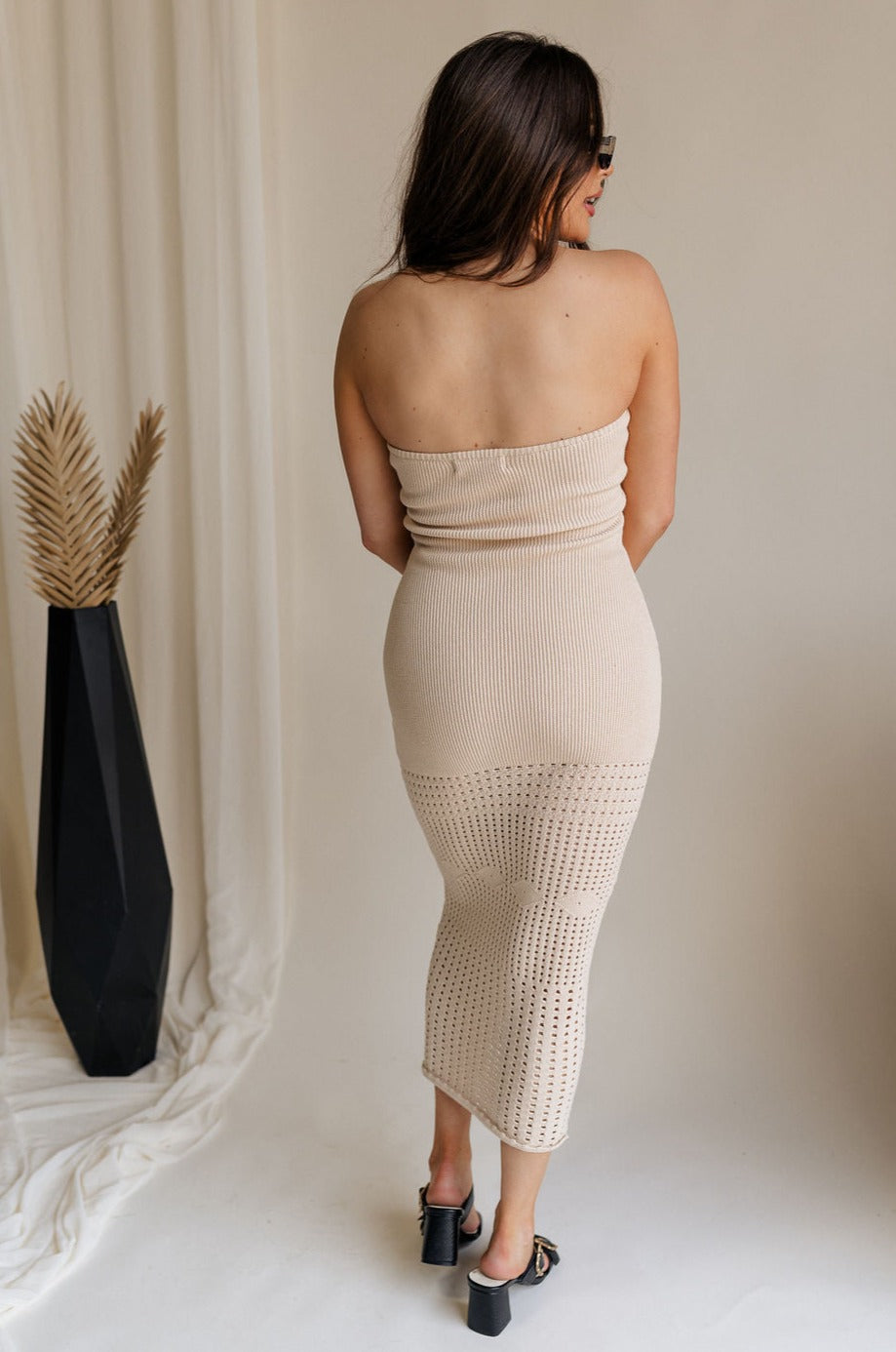 Full body back view of female model wearing the Camila Oat Strapless Knit Midi Dress which features Oat Knit Fabric, Midi Length, Strapless and Open Knit Design Hem