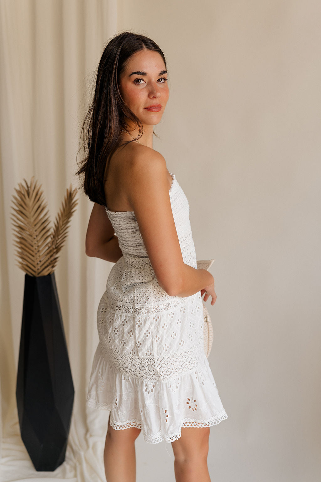 side view of female model wearing the Lucia White Eyelet Strapless Mini Dress which features White Eyelet Pattern, White Lining, Mini Length, Flare Hem Skirt and Strapless