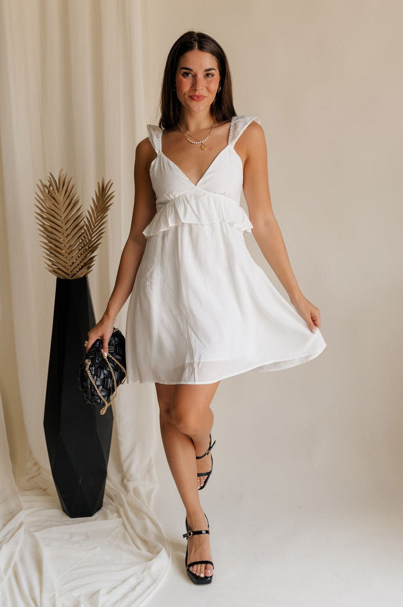 Full body view of female model wearing the Noelle White Ruffle Plunge Neckline Mini Dress which features White Lightweight Fabric, White Lining, Mini Length, Ruffle Details, V-Neckline and Smocked Back