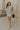 Full body front view of female model wearing the Gabriella Cream & Black Striped Mini Dress that has cream fabric with horizontal black stripes, a sleeveless body, round neck, and side pockets.