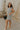 Full body side view of model wearing the Gabriella Cream & Black Striped Mini Dress that has cream fabric with horizontal black stripes, a sleeveless body, round neck, and side pockets.