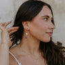 Side view of female model wearing the Paulina Red, White, & Blue Drop Earrings that have a red rhinestone sphere followed by white and blue spheres with gold wire between.