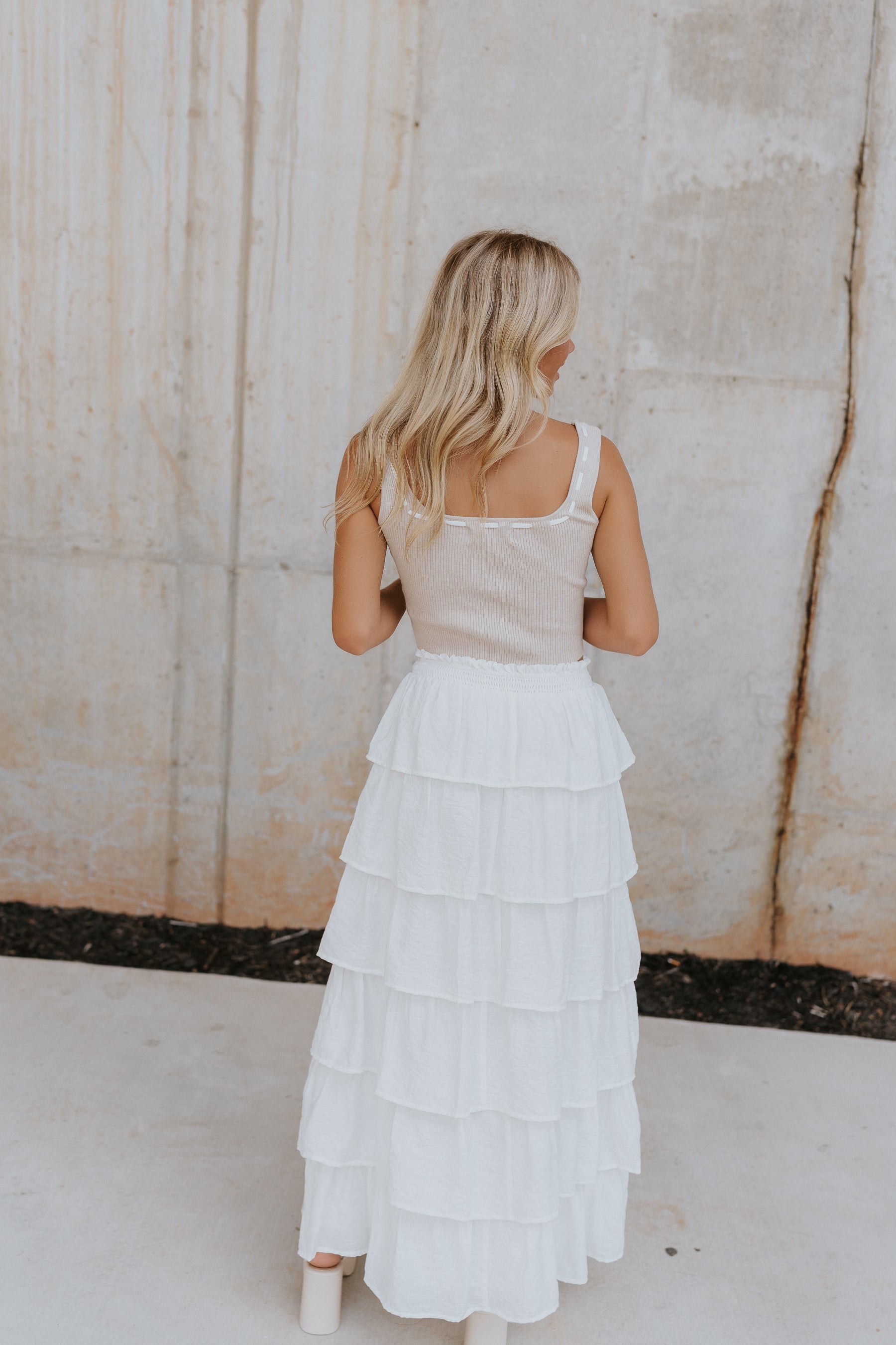 Back view of female wearing the Koda Cropped Tie Tank features a sleeveless tank with the square neck lined in an ivory weaved pattern and a front tie.