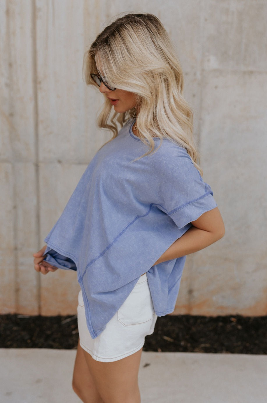 Side view of female model wearing the Nova Thread Short Sleeve Top which features Cotton Fabric, Curved Hem Details, Round Neckline and Shorts Sleeves. the top is available in blue and white