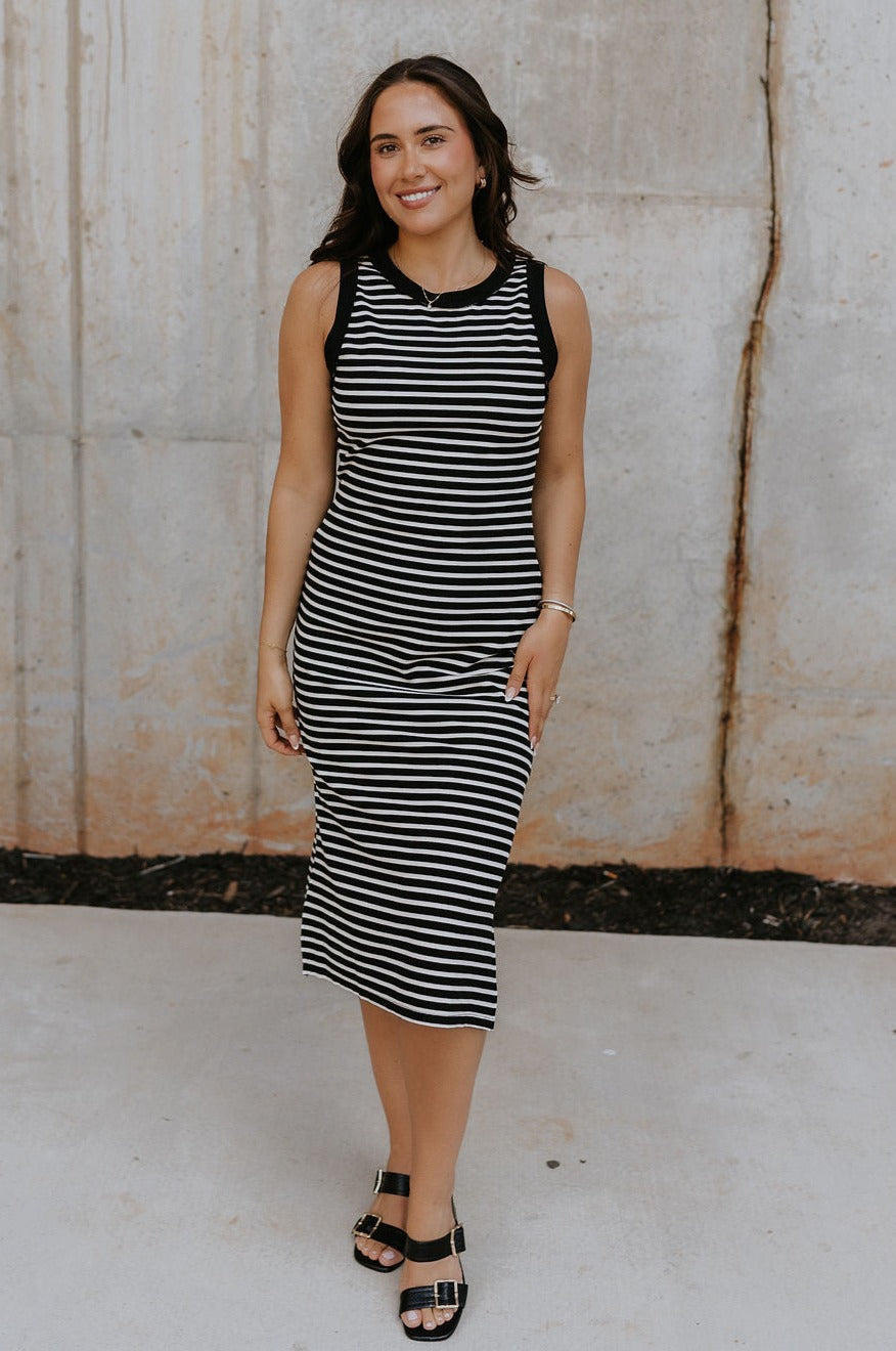 Full body view of female model wearing the Andri Black & White Stripe Midi Dress which features Black and Cream Stripe Pattern, Midi Length, Slits On Each Side, Round Neckline and Sleeveless