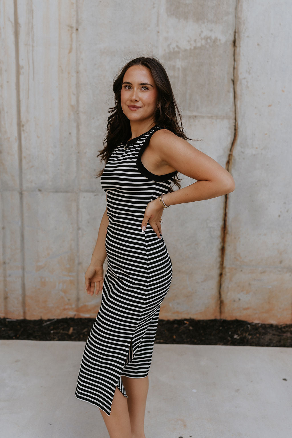 Side view of female model wearing the Andri Black & White Stripe Midi Dress which features Black and Cream Stripe Pattern, Midi Length, Slits On Each Side, Round Neckline and Sleeveless