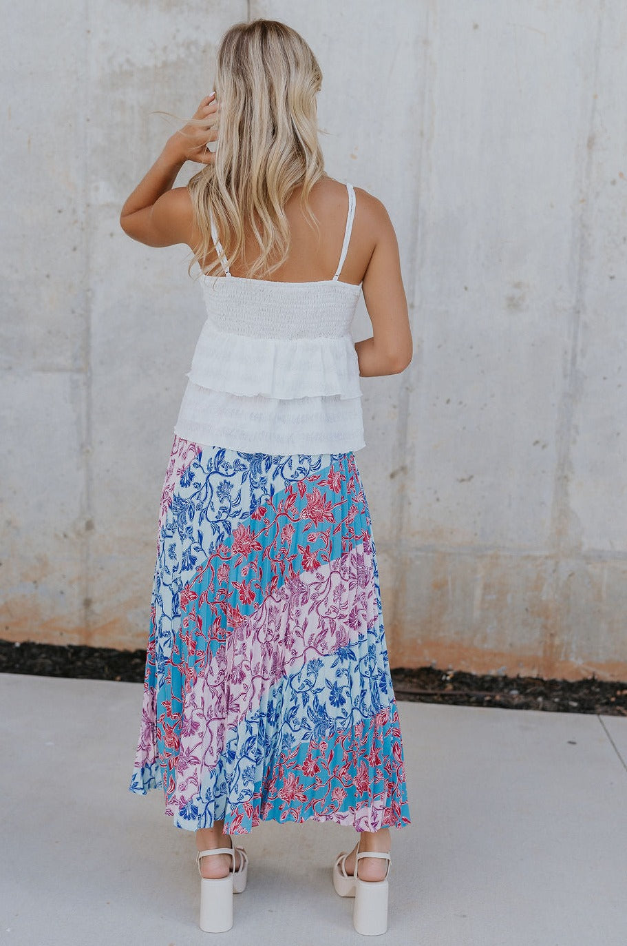 Back view of female model wearing the Lily Aqua & Pink Multi Pleated Maxi Skirt which features Blue, Pink, Red, Purple and Aqua Floral Print, Satin Pleated Fabric, Maxi Length, Light Blue Lining and Side Zipper with Hook Closure