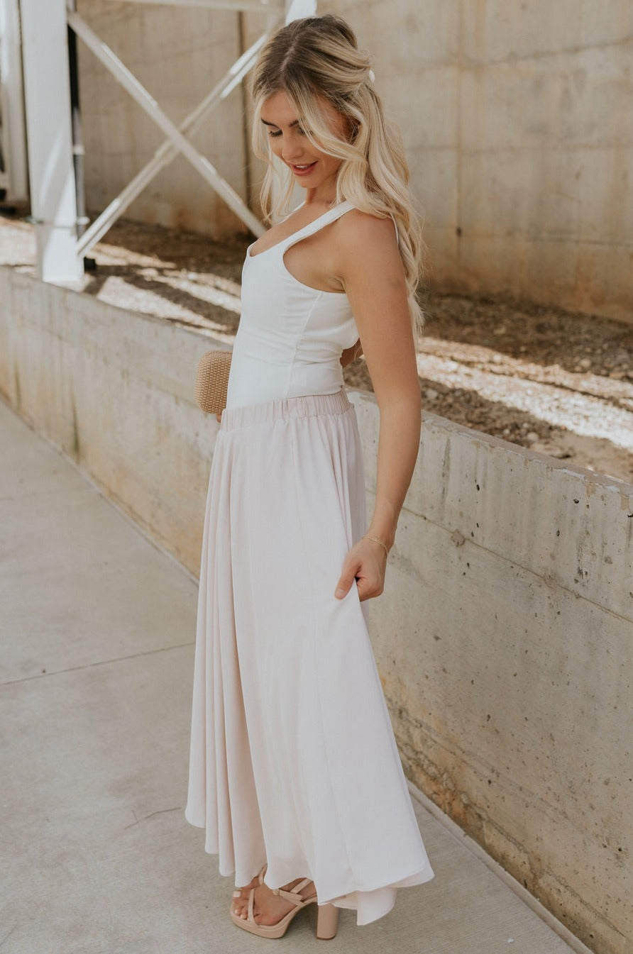 Full body side view of female model wearing the Mira Scooped Back Sleeveless Bodysuit which features Square Neckline, Thick Straps, Scoop Back and Thong Bottom with Button Snap Closure. the bodysuit is available in black and white