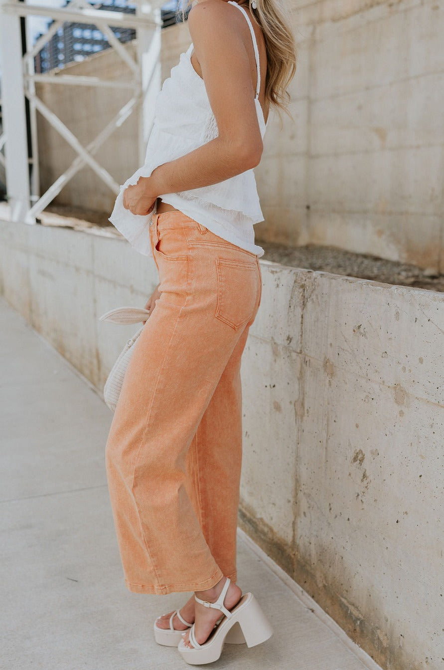 Side view of female model wearing the Kennedy Apricot Orange Wide Leg Pants which features Orange Denim Stretch Fabric, Cropped Wide Pant Leg, Front Zipper with Button Closure, Belt Loops, Two Front Pockets andTwo Back Pockets