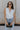 Front view of female model wearing the Emilia Satin Plunge Neckline Sleeveless Bodysuit which features Satin Fabric, Surplice Neckline with Button Snap, Sleeveless and Thong Bottom with Button Closure. the bodysuit is available in taupe and white