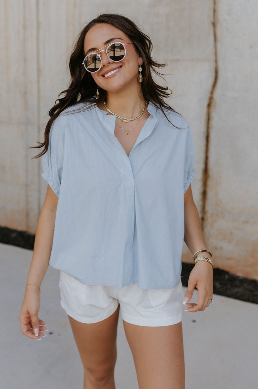 Front view of female model wearing the Noelle Chambray Blue Short Sleeve Top which features Light Blue Cotton Fabric, Slight Cropped Waist, Short Puff Sleeves and V-Neckline