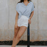 Full body view of female model wearing the Noelle Chambray Blue Short Sleeve Top which features Light Blue Cotton Fabric, Slight Cropped Waist, Short Puff Sleeves and V-Neckline