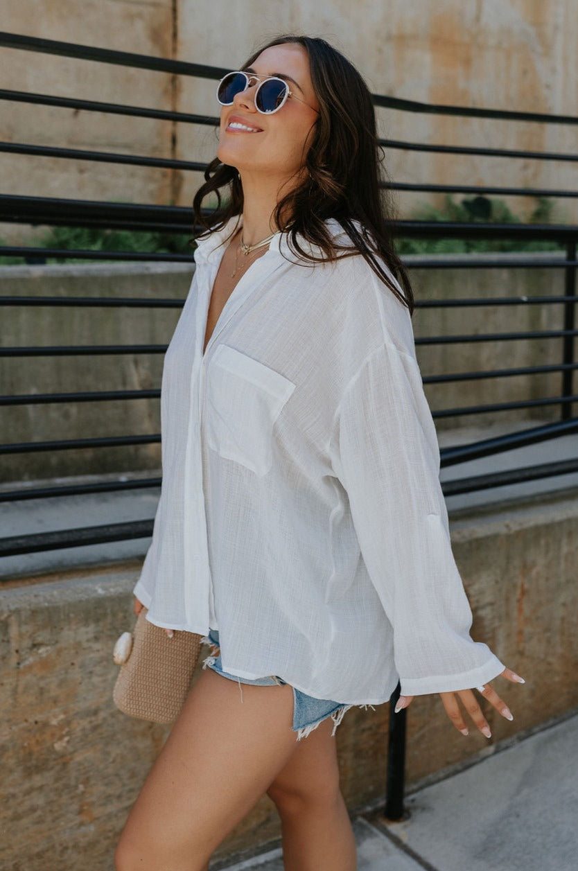 Side view of female model wearing the Alaina White Front Button-Up Long Sleeve Top which features White Lightweight Fabric, Front Button-Up Closure, Left Front Chest Pocket, Collared Neckline and Long Sleeves with Buttoned Cuffs