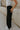 side view of female model wearing the Serena Black Cargo Drawstring Pants which features Black Lightweight Fabric, Jogger Pant Legs with Drawstring Ties, Cargo Pockets with Tortoise Buttons and Smocked Elastic Waistband