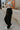 side view of female model wearing the Serena Black Cargo Drawstring Pants which features Black Lightweight Fabric, Jogger Pant Legs with Drawstring Ties, Cargo Pockets with Tortoise Buttons and Smocked Elastic Waistband