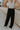 back view of female model wearing the Serena Black Cargo Drawstring Pants which features Black Lightweight Fabric, Jogger Pant Legs with Drawstring Ties, Cargo Pockets with Tortoise Buttons and Smocked Elastic Waistband