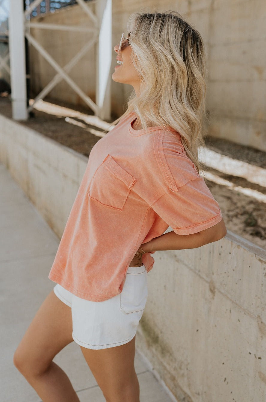 Side view of female model wearing the Ada Washed Cotton Short Sleeve Top which features Washed Cotton Fabric, Short Sleeves, Textured Thread Hem Details, Left Front Chest Pocket and Round Neckline