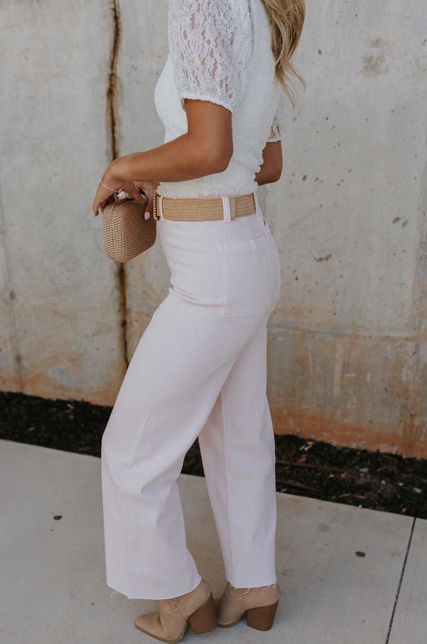 side view of female model wearing the Charli Cropped Wide Leg Pants which features Denim-Like Fabric, Wide Pant Legs, Raw Hem, Monochrome Front Button with Zipper Closure, Two Front Pockets, Two Back Pockets and Belt Loops. the pants are available in blue and pink.