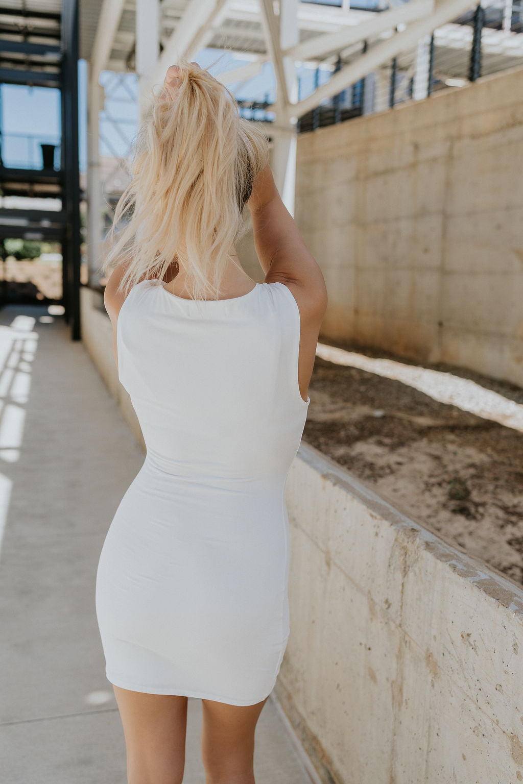 back view of female model wearing the Demi White & Black Bows Sleeveless Mini Dress which features White Lightweight Fabric, White Lining, Mini Length, Black Ribbon Bows Detail, Upper Cutout Details, Round Neckline and Sleeveless