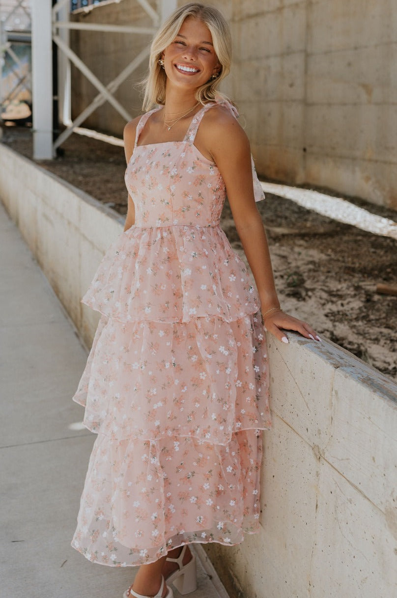 Full body view of female model wearing the Evie Peach Blush Floral Tiered Midi Dress which features Light Peach Sheer Fabric, Floral Print, Tiered Design, Midi Length, Light Peach Lining, Square Neckline, Tie Straps and Smocked Back