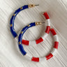 Image shows Eleanor Red, White, & Blue Hoop Earrings on top of each other against a white background. Earrings feature red and white striped and a blue section with gold stars.