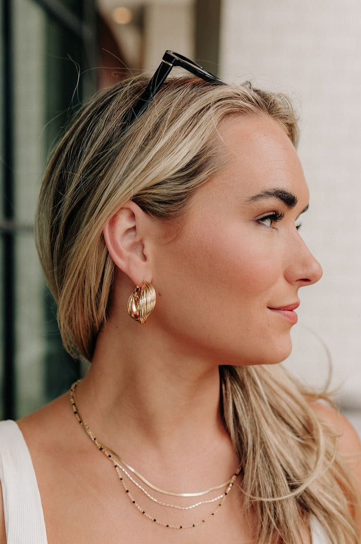 Side view of female model wearing the Briana Gold Twisted Hoops that have twisted gold metal hoops on hinge backs.