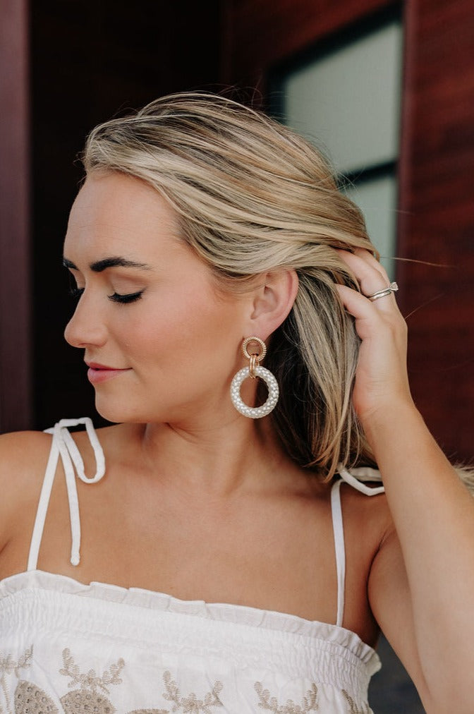 Side view of female model wearing the Skyler White & Gold Dangle Earrings that have gold circles attached to white dangle circles.